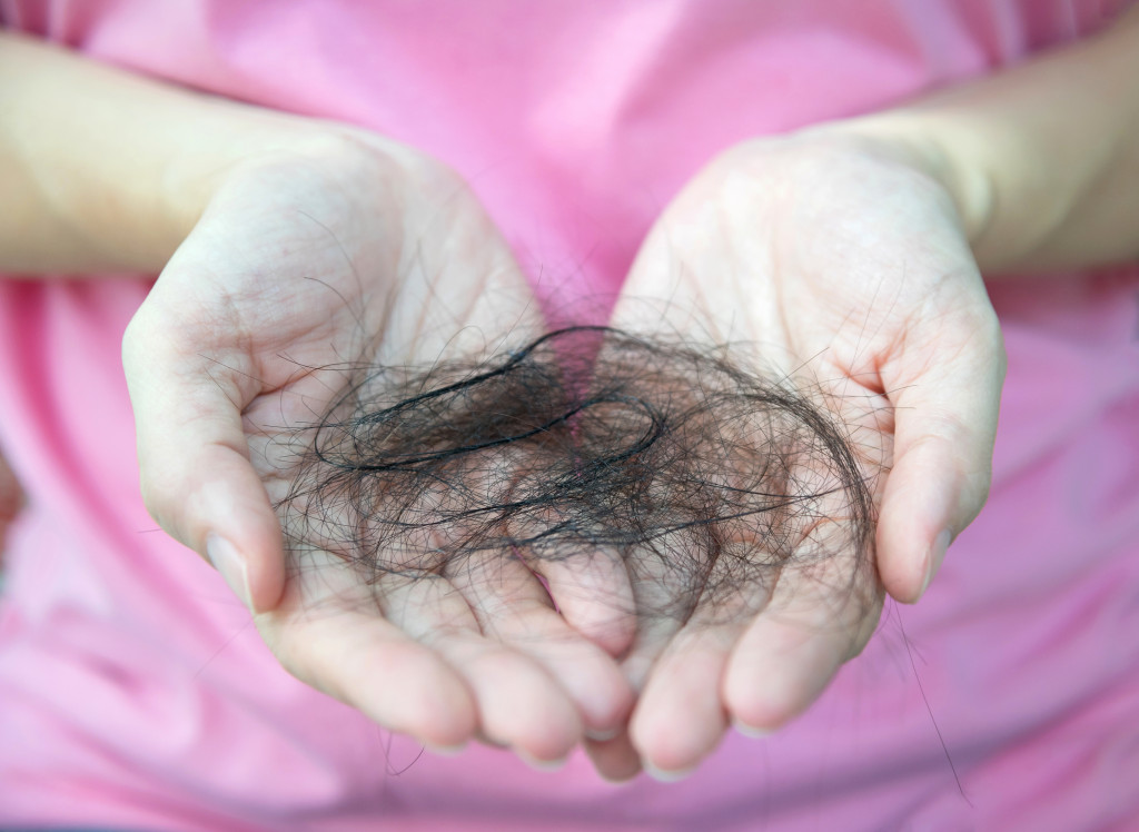 Close-up of woman hand in pink t-shirt hold loss hair